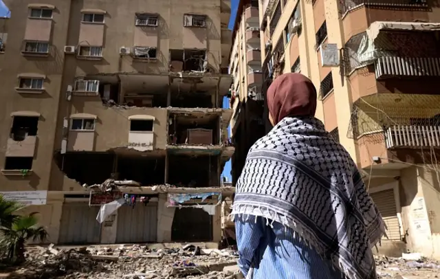 A Palestinian woman wearing a traditional keffiyeh scarf looks for belongings to salvage among the rubble of a building following Israeli air strikes in Gaza City