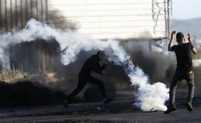 Palestinian protesters seek cover from tear gas during clashes with Israeli troops at a checkpoint near the West Bank City of Nablus. Photo: 15 May 2021