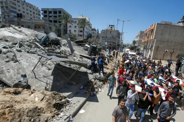 Mourners carry the bodies of Palestinians who were killed amid a flare-up of Israeli-Palestinian violence near the remains of a building destroyed in Israeli air strikes at the Beach refugee camp, in Gaza City on 15 May 2021