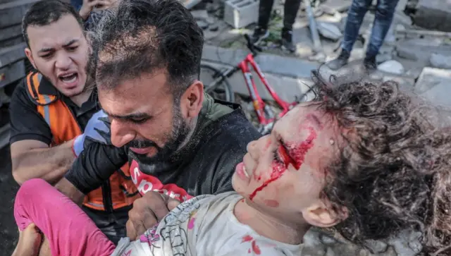 A Palestinian father carries his injured daughter from the rubble of a destroyed house after an Israeli air strike in Gaza City, 16 May 2021.