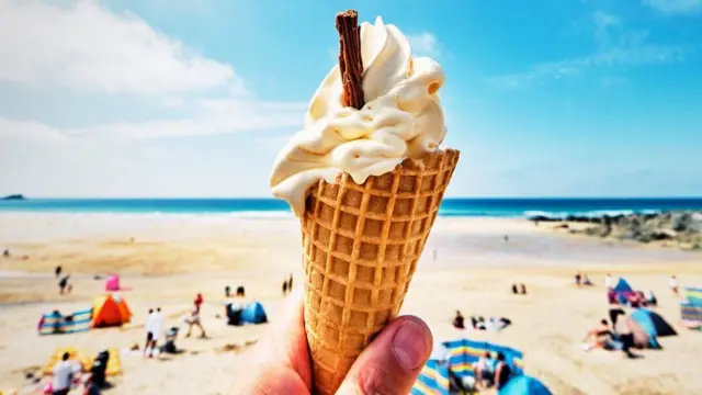 A stock image of someone holding an ice cream cone on a beach