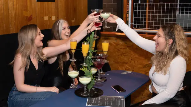 Three women raise a glass in a bar