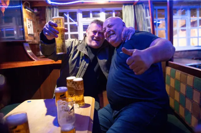 Two men raise a pint glass as pubs serve indoors once more