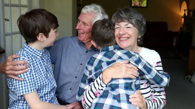 A family of two boys and an older couple hug