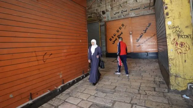 Two people walk past closed shops in the Old City of Jerusalem