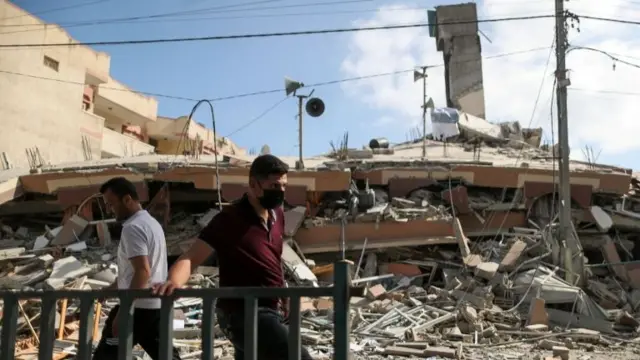 Palestinians walk past the remains of a building in Gaza City after it was destroyed in Israeli air strikes (18 May 2021)