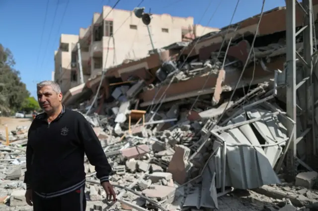 A Palestinian man stands near the remains of a building after it was destroyed in Israeli air strikes