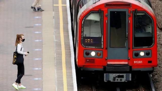 A person on a train platform while a Tube train pulls up alongside