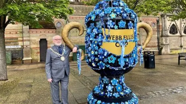 Mayor next to Webb Ellis Cup covered in forget-me-nots