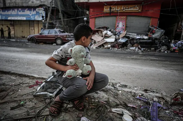 A boy is seen with his teddy bear at damaged site after Israeli army carried out airstrike over a building in Sheikh Ridvan neighbourhood in Gaza City,