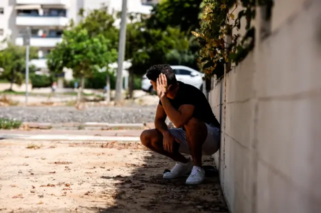 A man takes cover as a siren warning of incoming rockets launched from the Gaza Strip towards Israel sounds, in Ashkelon, Israel, on 20 May 2021