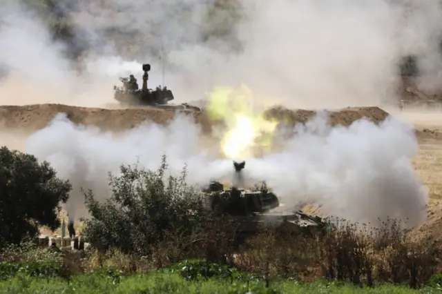 An Israeli soldier stands nearby as an artillery unit fires near the border between Israel and the Gaza Strip, as seen on the Israeli side May 20, 2021