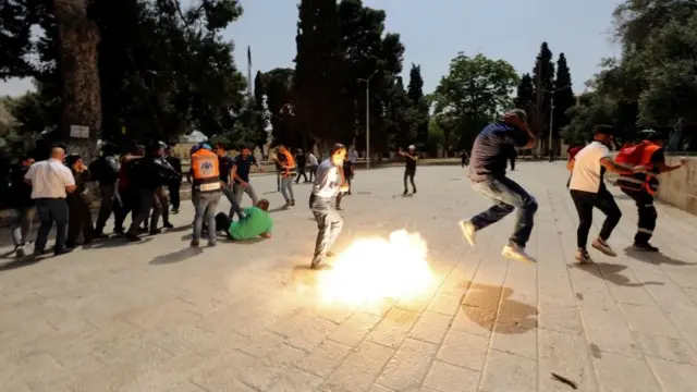 Palestinians jump as a stun grenade explodes during clashes with Israeli police near the al-Aqsa mosque in Jerusalem