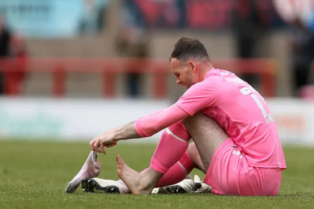 Tranmere keeper Joe Murphy puts his sock back on