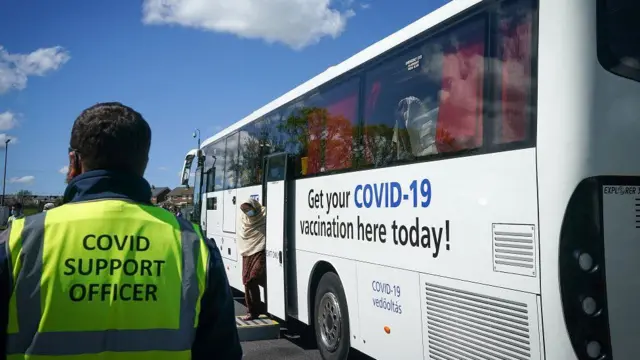 A Covid support officer standing next to a bus offering vaccinations