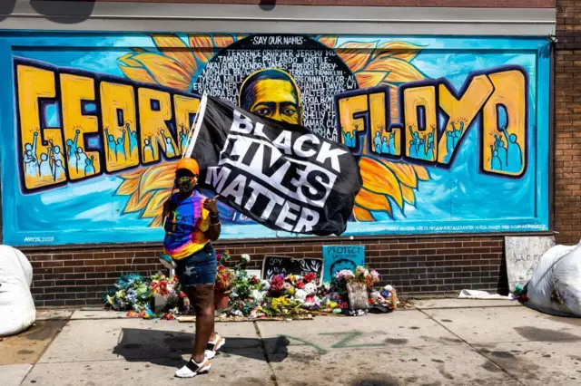 A woman holds a Black Lives Matter flag front of a mural of George Floyd near the George Floyd Memorial Square on May 25, 2021 in Minneapolis, Minnesota