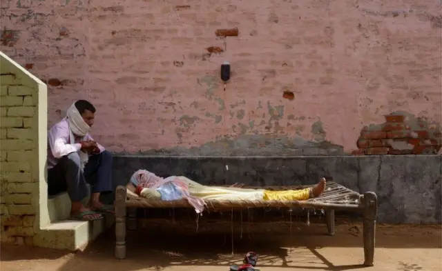 A man sits next to his wife, suffering from fever, in a village in India