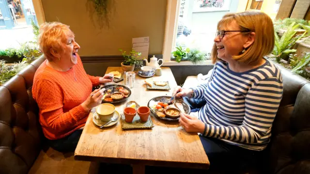 Two people laughing as they enjoy food in a restaurant