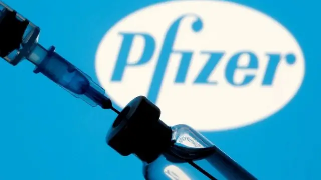A vial of vaccine in front of a Pfizer sign