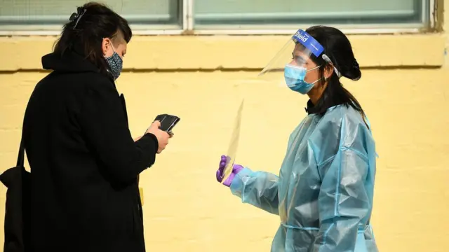 A health worker in full protective equipment holds up a sign for a woman outside a testing clinic