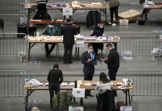 Election agents with clipboards watch votes being counted