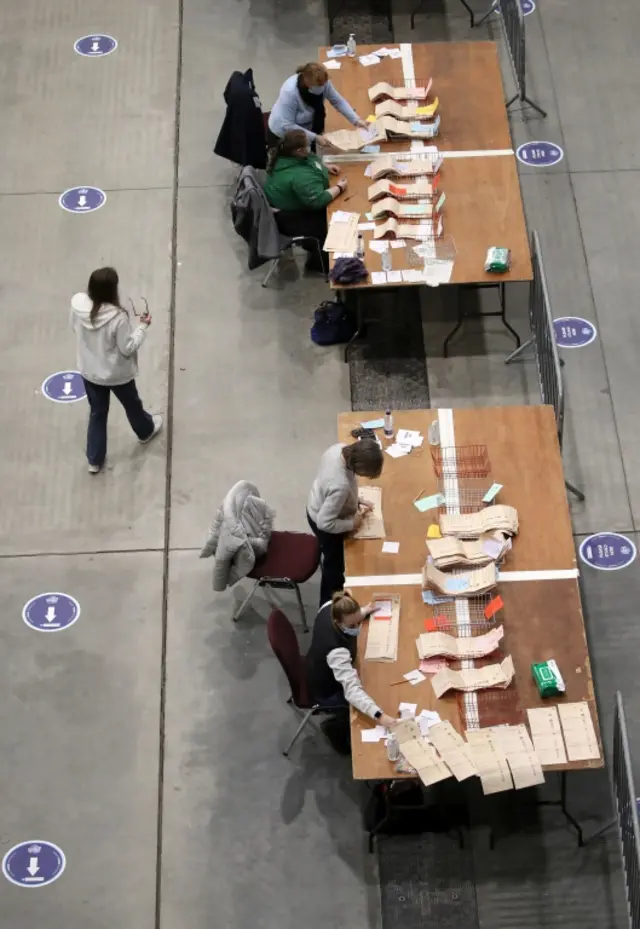 Four women count votes on two separate desks, covered with piles of ballot papers in wire trays