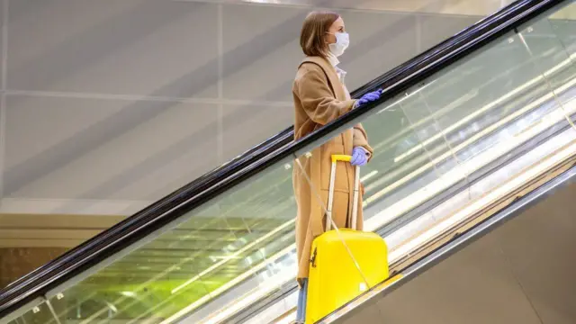 A woman stands on an escalator with a suitcase