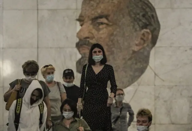 People wearing face masks walk in front of a portrait of Soviet Union founder Vladimir Lenin at the Metro station Biblioteka Lenina in Moscow, Russia, on 18 June 2021