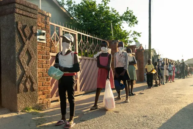 A queue of needy individuals with plates in hand forms outside Samantha Murozoki's home in Chitungwiza