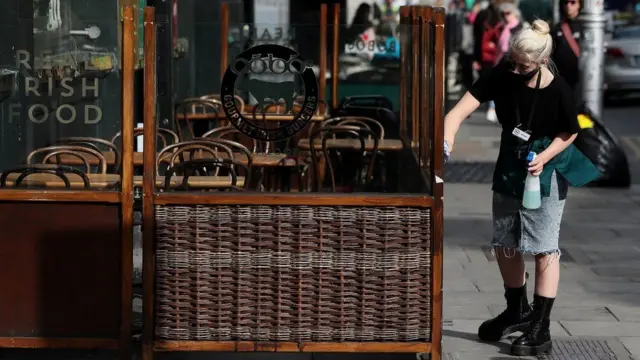 A woman cleans the outside seating area of a restaurant