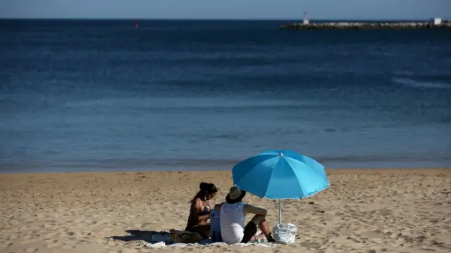 Two people sitting under an umbrella on a beach