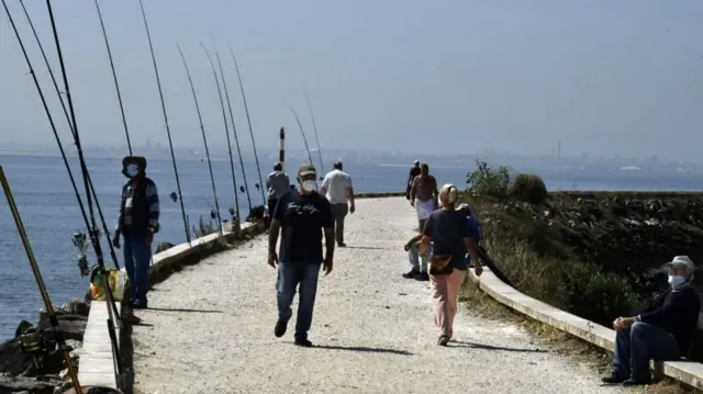 People wear masks while walking on the coast in Lisbon