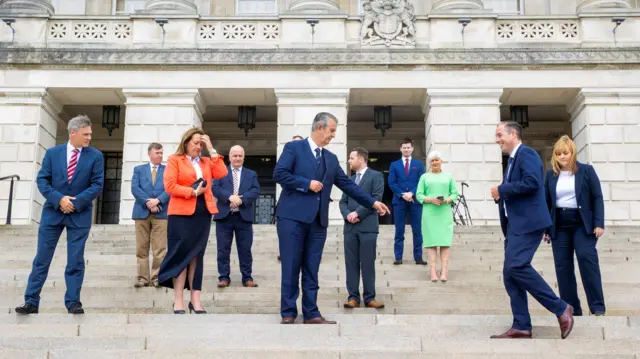 DUP leader Edwin Poots (centre) directs First Minister designate Paul Givan where to stand on the steps on Stormont during a photocall with part of Mr Poots first ministerial team.