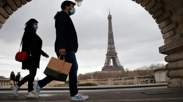 A couple wearing protective face masks walk past the Eiffel Tower