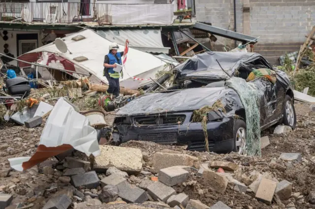 A firefighter inspects a destroyed car amid debris and damaged houses hit by the floods in Schuld near Bad Neuenahr, western Germany