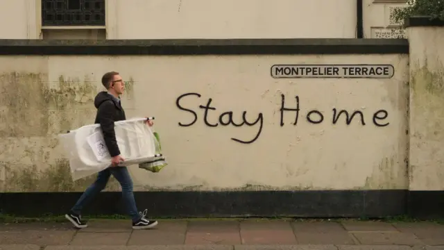 Someone walking past some graffiti saying: 'stay home'