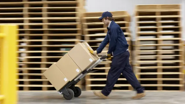 Worker pushing trolley in warehouse - stock photo