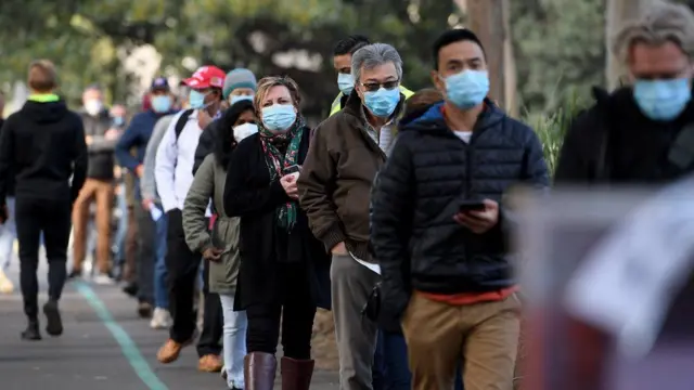 People wearing face masks queue in the street in Sydney, Australia