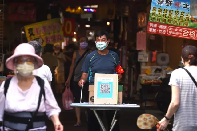 A member of staff stands at the entrance of a market making sure people are registered before shopping at the market in Taipei