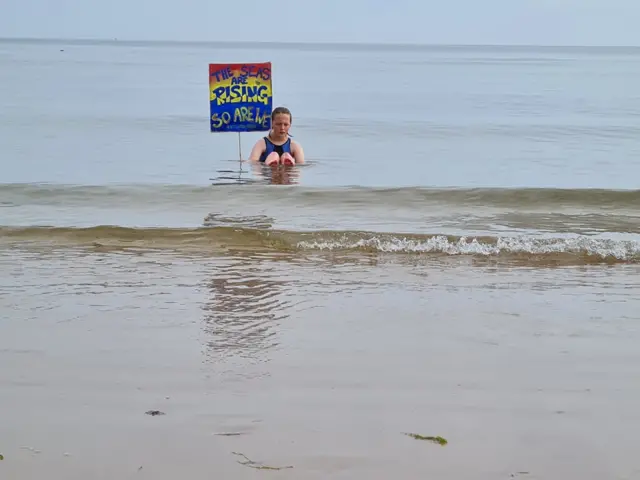 One protester sits in sea with a placard