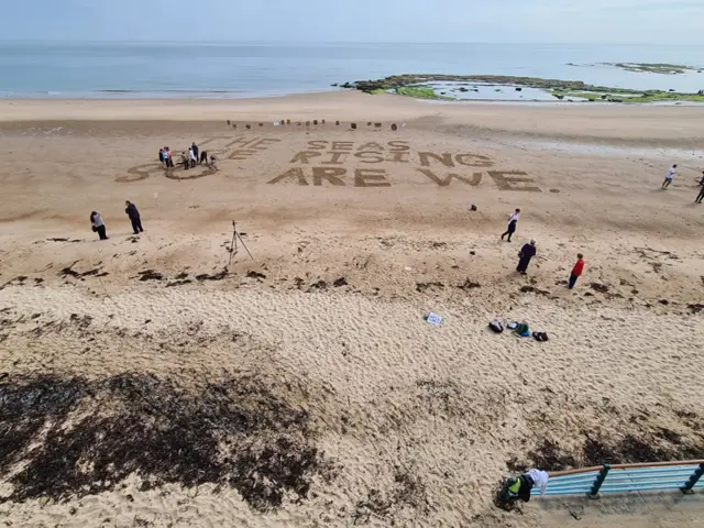 Slogan 'the seas are rising, so are we' written in the sand