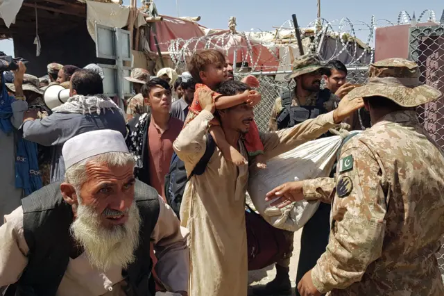 Pakistani soldiers (R) check stranded Afghan nationals at the Pakistan-Afghanistan border crossing point in Chaman on August 13, 2021