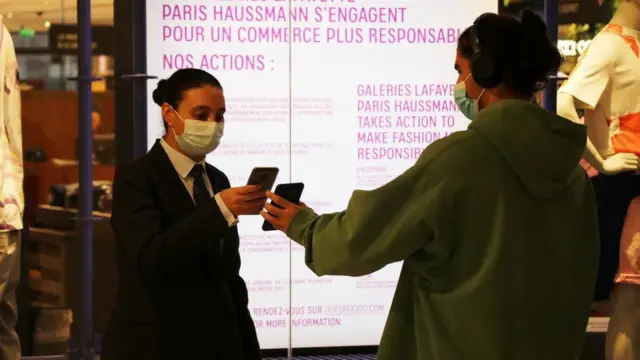 Woman checks a member of the public's health pass outside a shop in France