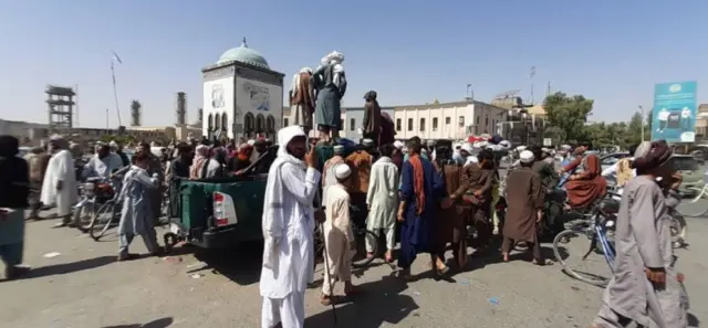 Afghans look on as Taliban militants gather around the main square after taking control of Kandahar