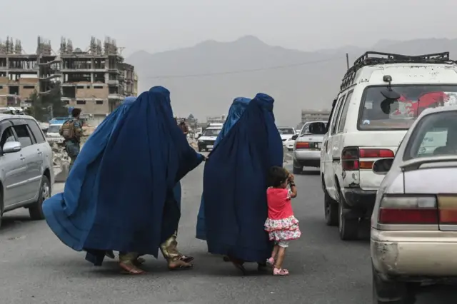 Women wearing burkas cross the road in Kabul