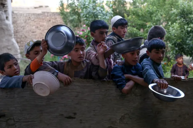 Afghan children hold plates out as they wait to receive food