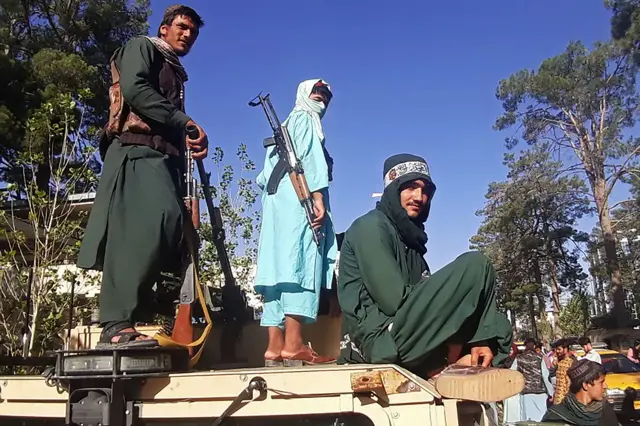 Taliban fighters stand on a vehicle along the roadside in Herat