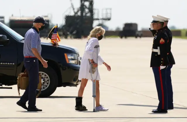 Wearing a boot and supported by a crutch, first lady Jill Biden if followed by U.S. President Joe Biden as they board Marine On