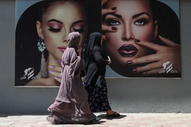 Burqa clad women walk past a billboard put up on the wall of a beauty salon in Kabul on 7 August, 2021