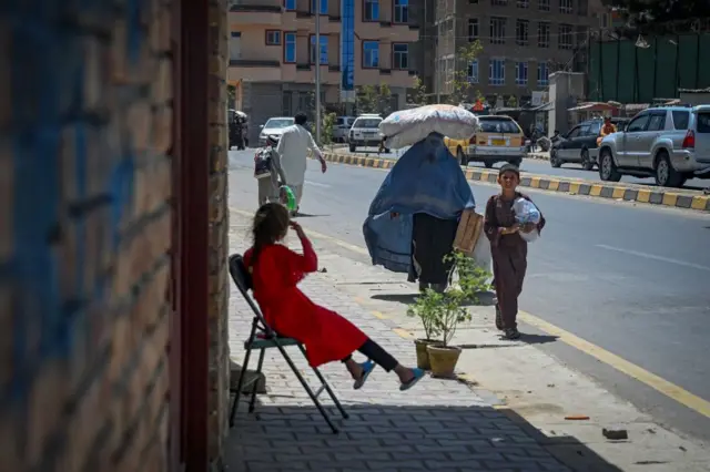 A burka-clad woman carrying a sack on her head walks along a road in Kabul on 7 August 2021